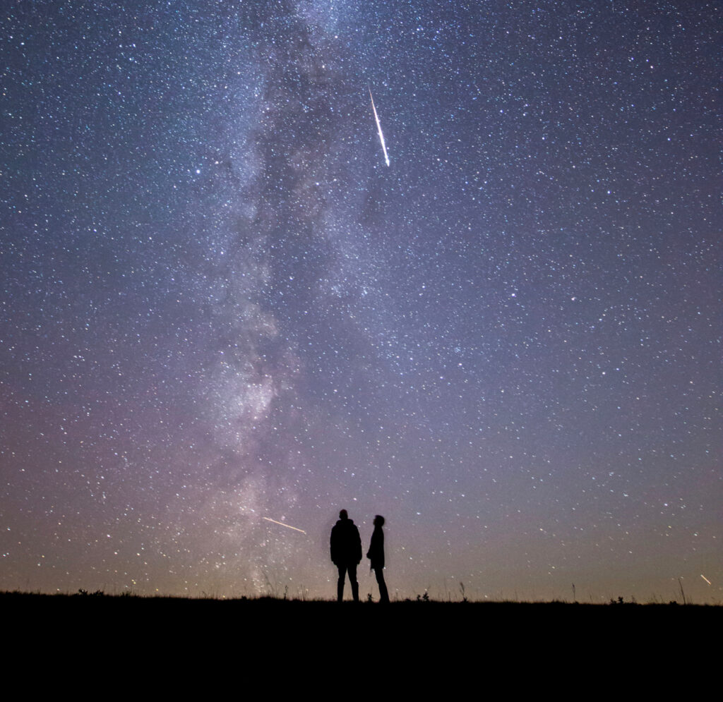 Zwei Menschen unterm Sternenhimmel mit Milchstrasse und Sternschnuppe